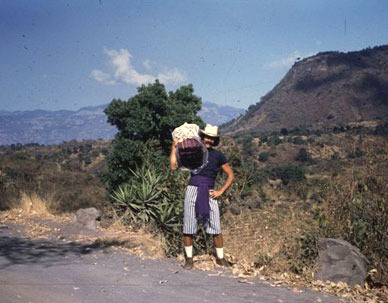 Standing on a mountain side with fabric slung over right should on a sunny date at Lake Atitlan